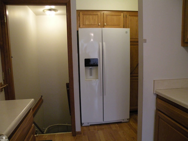 kitchen with brown cabinetry, white refrigerator with ice dispenser, light countertops, and light wood finished floors