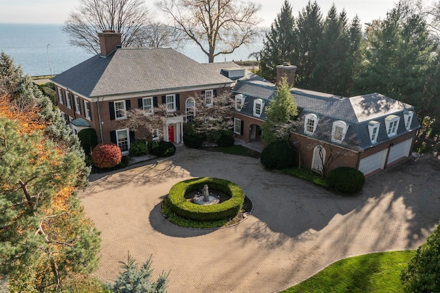 view of front of house featuring a garage, brick siding, curved driveway, and a chimney