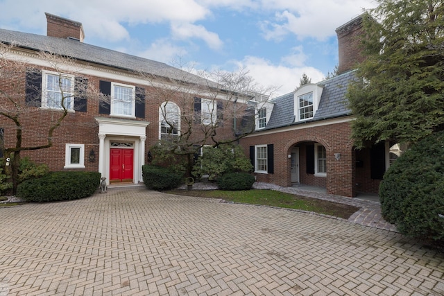 view of front of property featuring a high end roof, a chimney, and brick siding