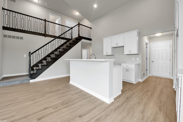 kitchen featuring light wood-style floors, baseboards, a high ceiling, and visible vents