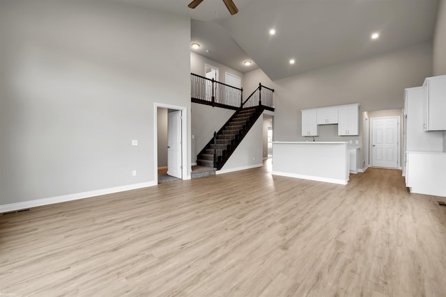 unfurnished living room featuring stairway, light wood-style floors, ceiling fan, high vaulted ceiling, and baseboards