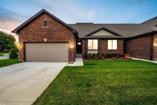 ranch-style home with brick siding, a shingled roof, an attached garage, driveway, and a front lawn