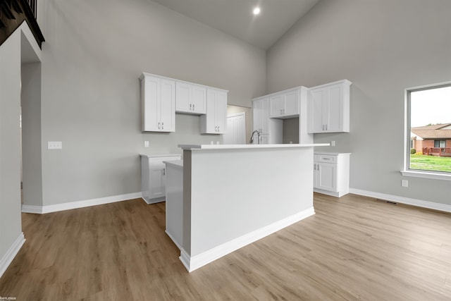 kitchen with an island with sink, white cabinetry, a high ceiling, and baseboards