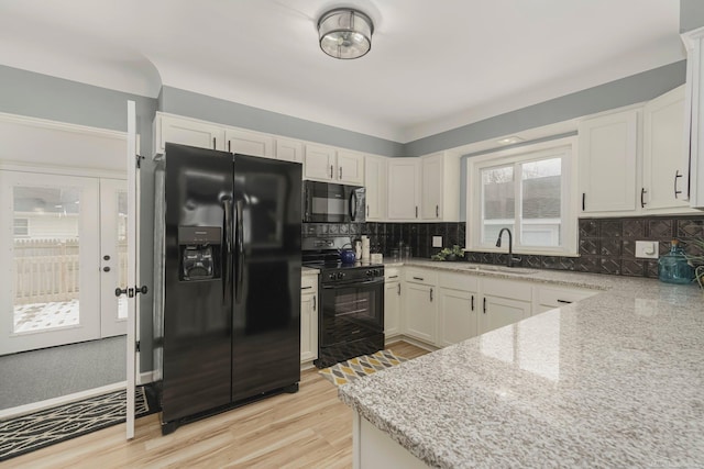 kitchen with black appliances, tasteful backsplash, a sink, and light wood-style floors