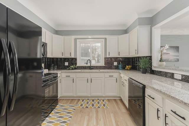 kitchen with white cabinets, light wood-style flooring, a sink, black appliances, and backsplash