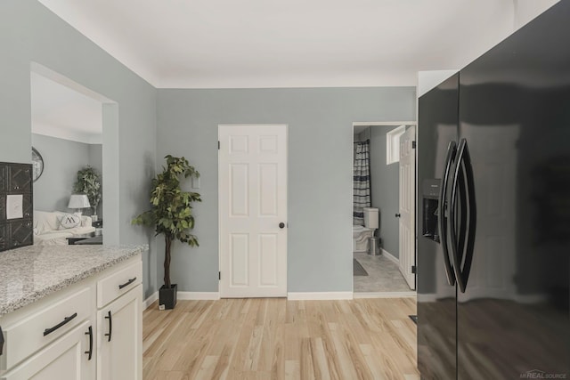 interior space with light wood finished floors, baseboards, white cabinets, light stone counters, and black refrigerator with ice dispenser