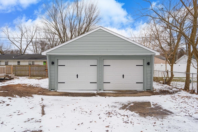 snow covered garage featuring a garage and fence