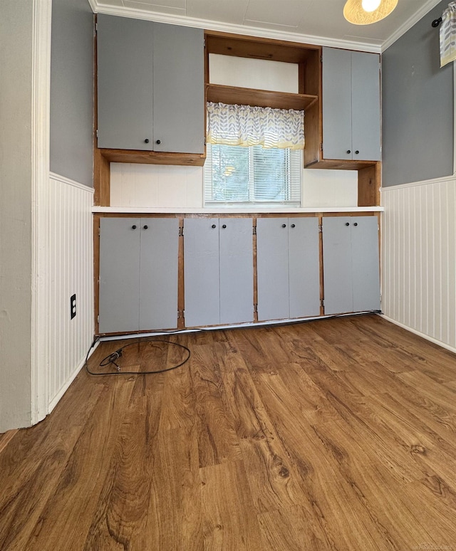 kitchen featuring a wainscoted wall, wood finished floors, gray cabinets, crown molding, and open shelves