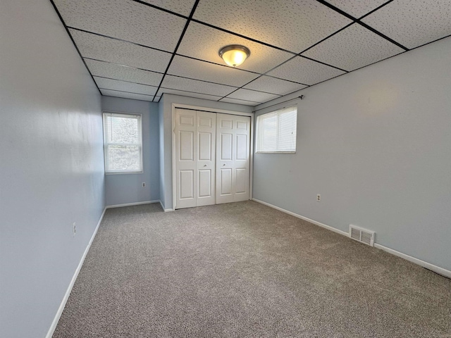 unfurnished bedroom with a drop ceiling, carpet floors, visible vents, baseboards, and a closet