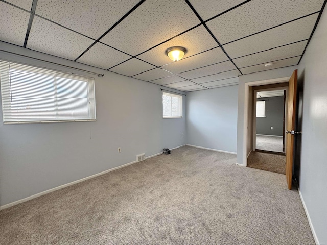 empty room featuring a paneled ceiling, carpet floors, baseboards, and visible vents