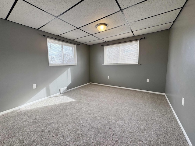 carpeted spare room featuring visible vents, a drop ceiling, and baseboards