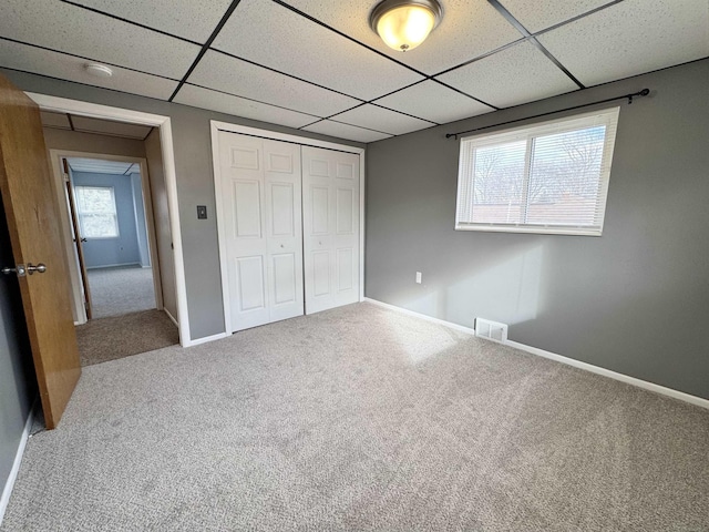 unfurnished bedroom featuring a drop ceiling, carpet flooring, visible vents, baseboards, and a closet