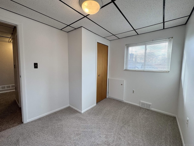 carpeted spare room featuring a drop ceiling, visible vents, and baseboards