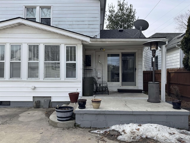 view of exterior entry featuring a shingled roof, crawl space, fence, and a patio