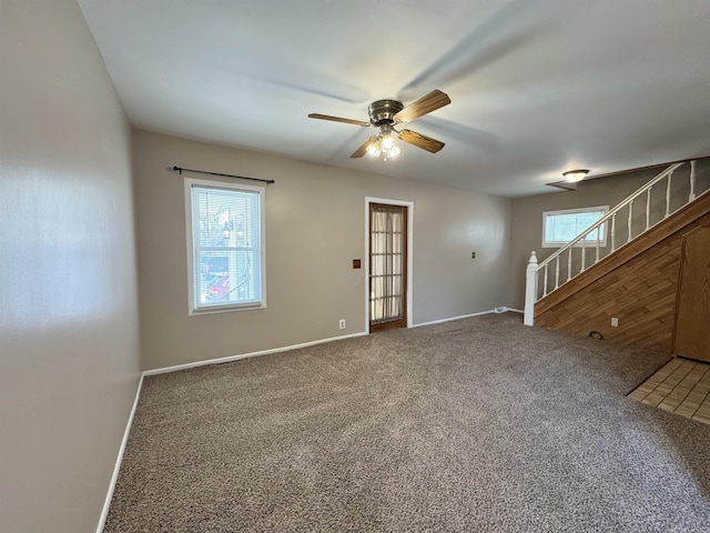 empty room featuring a ceiling fan, carpet flooring, baseboards, and stairs