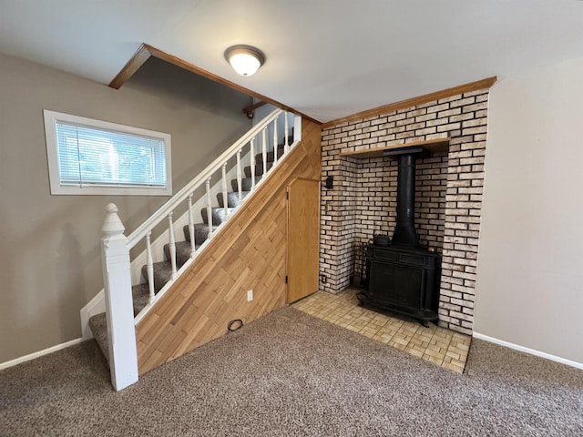 unfurnished living room with stairway, carpet flooring, a wood stove, and baseboards