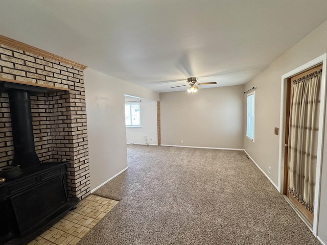 unfurnished living room with light carpet, ceiling fan, a wood stove, and baseboards