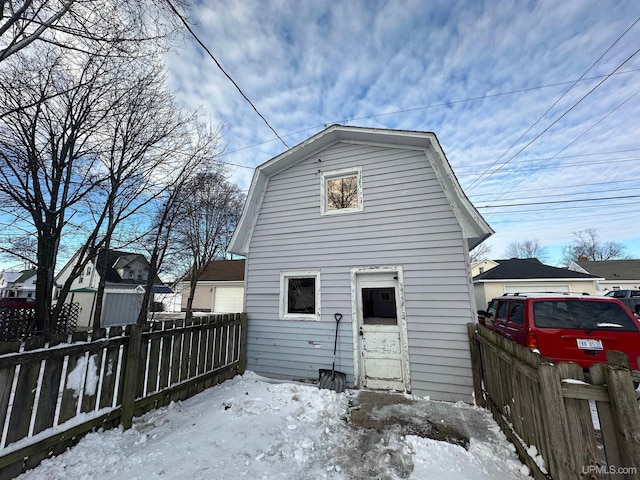 snow covered house featuring fence private yard and a gambrel roof