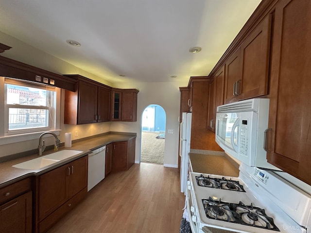 kitchen featuring arched walkways, light wood-style floors, glass insert cabinets, a sink, and white appliances