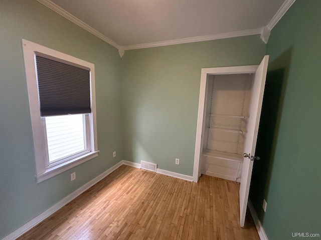 unfurnished room featuring crown molding, light wood-style flooring, visible vents, and baseboards