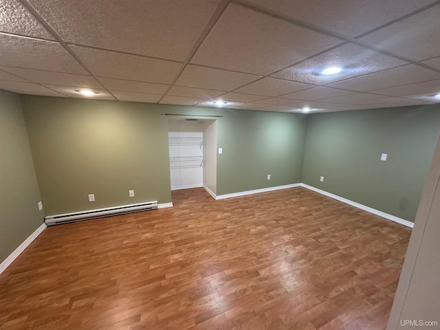 finished below grade area featuring baseboards, a drop ceiling, baseboard heating, and wood finished floors