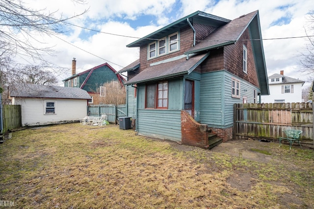 rear view of house featuring a lawn, a fenced backyard, roof with shingles, an outbuilding, and central air condition unit