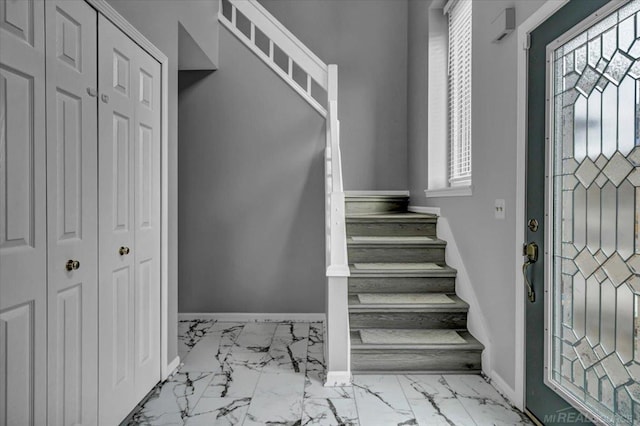 foyer with marble finish floor, stairs, and baseboards