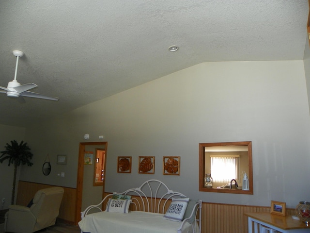 bedroom featuring high vaulted ceiling, wainscoting, and a textured ceiling