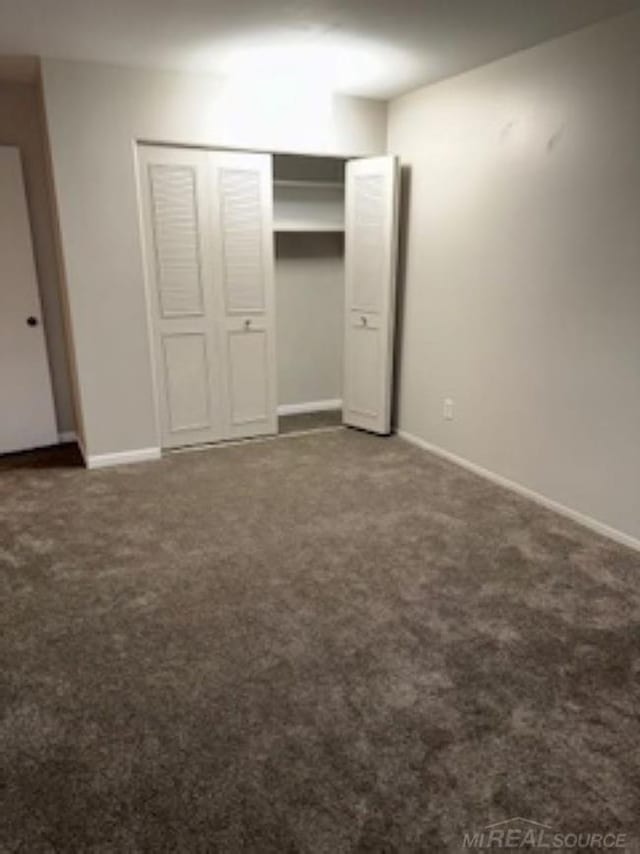 unfurnished bedroom featuring a closet, dark carpet, and baseboards