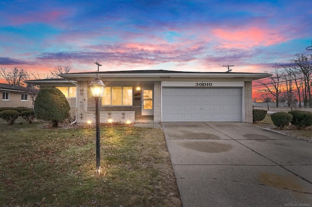 view of front of property featuring a garage, a yard, driveway, and brick siding