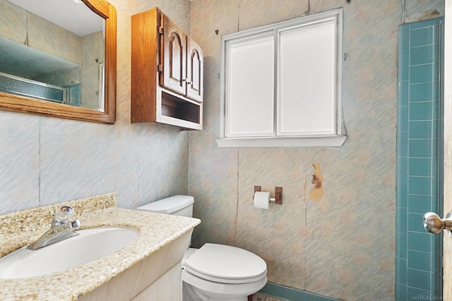 bathroom with a tile shower, vanity, and toilet