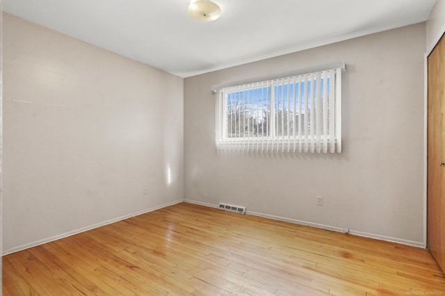 empty room featuring wood-type flooring, visible vents, and baseboards