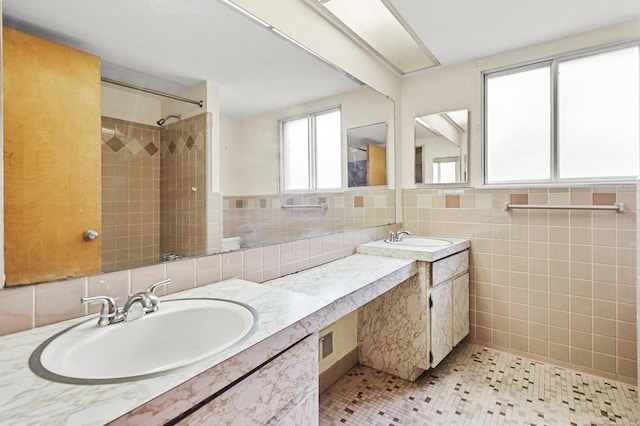 bathroom with a tile shower, double vanity, a sink, and tile walls