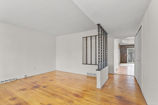 spare room with stairs, light wood finished floors, and visible vents