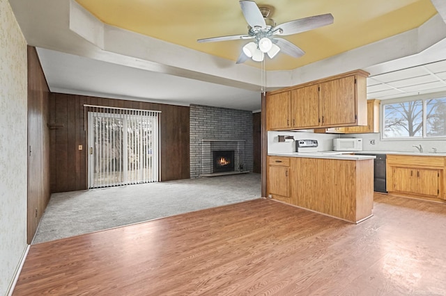 kitchen featuring light wood finished floors, white microwave, open floor plan, a peninsula, and light countertops