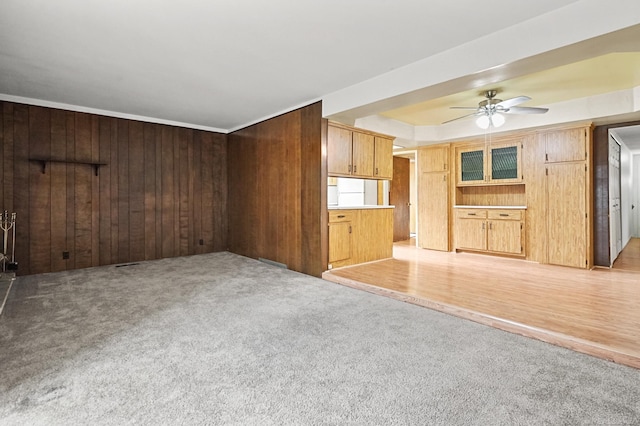 unfurnished living room with wood walls, a ceiling fan, and light colored carpet