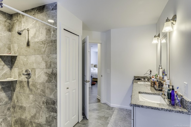 bathroom featuring marble finish floor, tiled shower, vanity, and baseboards