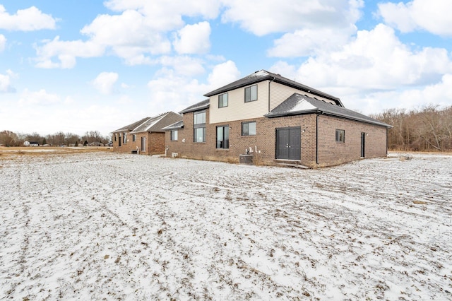 snow covered rear of property featuring central air condition unit and brick siding