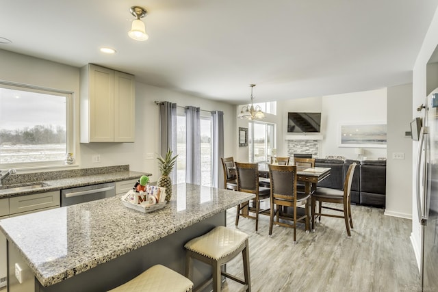 kitchen with a center island, light wood finished floors, appliances with stainless steel finishes, a sink, and light stone countertops