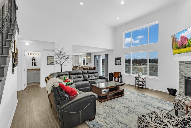 living area with a towering ceiling, wood finished floors, stairs, a stone fireplace, and a notable chandelier