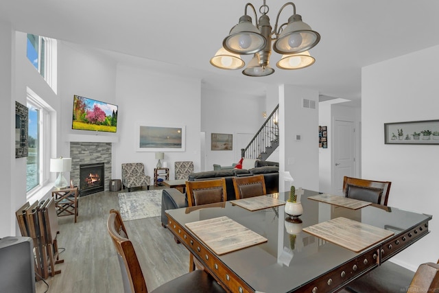 dining area with visible vents, stairway, wood finished floors, a fireplace, and a notable chandelier