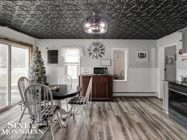 dining area with an ornate ceiling, a baseboard radiator, wainscoting, wood finished floors, and wallpapered walls