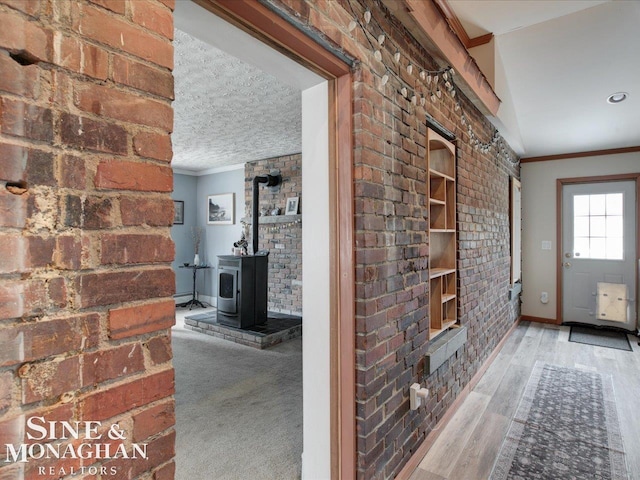 interior space featuring a wood stove, brick wall, crown molding, and wood finished floors