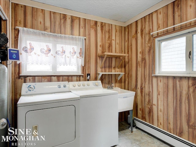 clothes washing area with laundry area, washer and clothes dryer, a baseboard radiator, a textured ceiling, and wood walls