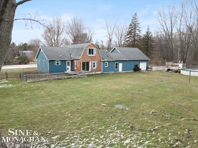 back of property with a garage, a gambrel roof, a chimney, fence, and a yard