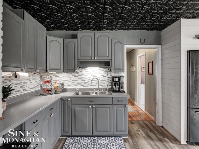 kitchen featuring light wood-style flooring, gray cabinetry, a sink, backsplash, and freestanding refrigerator