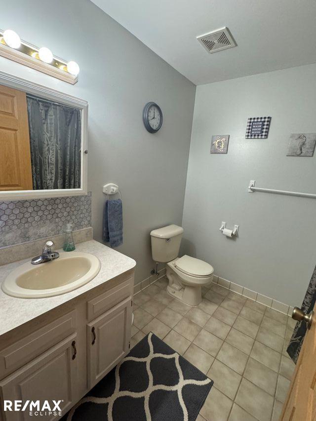 bathroom with visible vents, decorative backsplash, toilet, tile patterned flooring, and vanity