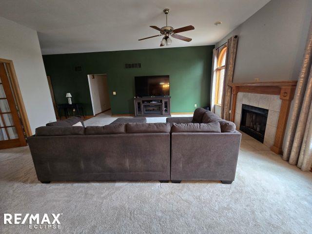 living area with light carpet, ceiling fan, a tile fireplace, and visible vents