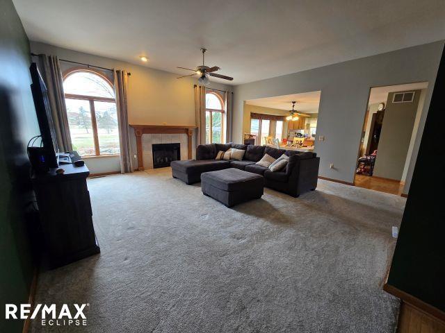 living area with visible vents, a tiled fireplace, a ceiling fan, carpet flooring, and baseboards