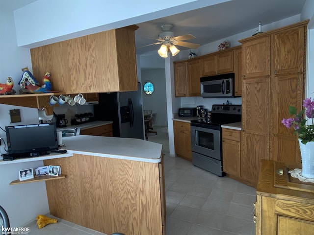 kitchen with light countertops, appliances with stainless steel finishes, brown cabinetry, a ceiling fan, and a peninsula